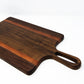 Medium size wood charcuterie board, made of a dark Walnut and two strips of dark reddish-brown Bubinga, with unique looped handle and exaggerated curves.