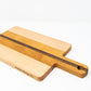 Small wood charcuterie board, made of light blonde Maple, golden-brown Cherry and a center strip of dark Walnut, with a timeless rectangular shape and a straight handle.