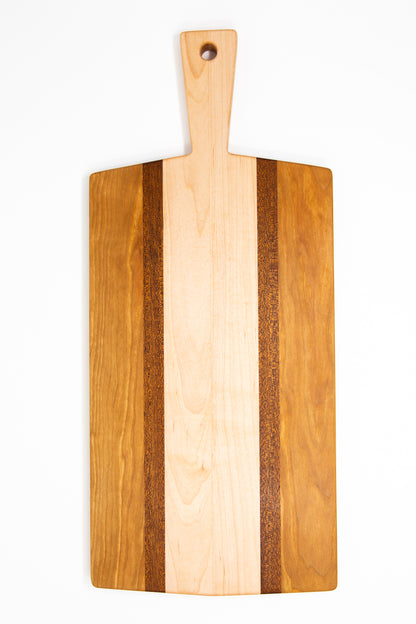 Large size wood charcuterie board, made of golden-brown Cherry, reddish brown Sapele and a center piece of light blonde Maple with a slightly tapered handle and a long rectangular body.