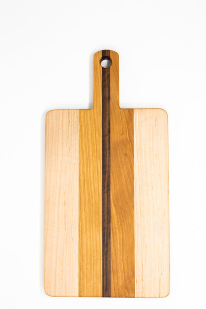 Small wood charcuterie board, made of light blonde Maple, golden-brown Cherry and a center strip of dark Walnut, with a timeless rectangular shape and a straight handle.