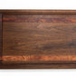 Medium size wood cutting board, made of dark walnut and two strips of dark reddish brown Bubinga, with a juice groove and side handles.