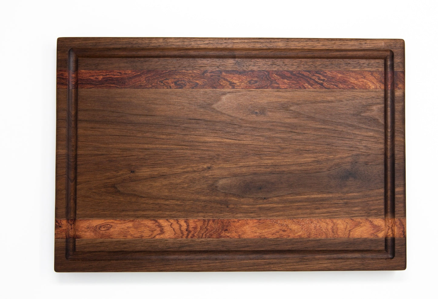 Medium size wood cutting board, made of dark walnut and two strips of dark reddish brown Bubinga, with a juice groove and side handles.