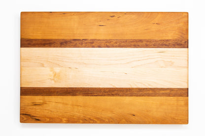 Large size wood cutting board, made of golden-brown Cherry, dark reddish-brown Sapele and light blonde Maple, with side handles.