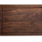 Small wood cutting board, made of dark Walnut, with a juice groove and side handles.