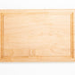 Small wood cutting board, made of light blonde Maple, with a juice groove and side handles.
